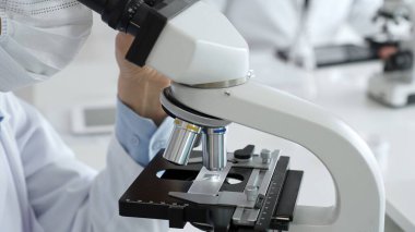 Laboratuar mikroskobunu dikkatlice ayarlayan koruyucu eldivenler giyen bilim teknisyeni titiz bir araştırma tekniği sergiliyor. Tıp, sağlık ve bilim konsepti