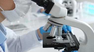 Mikroskop merceklerini inceleyen, detaylı tıbbi laboratuvar araştırmaları yapan mavi eldivenli eldiveni kapatın. Tıp, sağlık ve bilim konsepti.