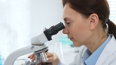 Kadın bilim adamı mikroskop örneklerini analiz ediyor, çağdaş laboratuvar ortamında gelişmiş ekipmanlarla tıbbi tedavileri araştırıyor. Tıp, sağlık ve bilim konsepti