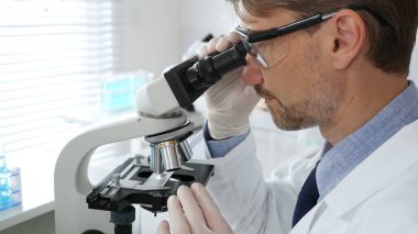 Korumalı giysiler giyerken bilimsel örnekleri analiz eden profesyonel bir araştırmacı, cam ekipmanlarla steril laboratuvar ortamında dikkatlice çalışıyor. Tıp, sağlık ve bilim konsepti