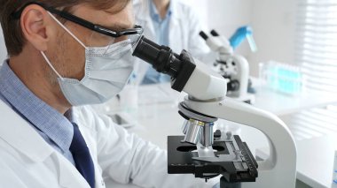 Tıbbi araştırmacı numuneyi mikroskop altında analiz ediyor steril laboratuvar ortamında koruyucu giysiler giyiyor ve bilimsel araştırmalar yapıyor. Tıp, sağlık ve bilim konsepti.