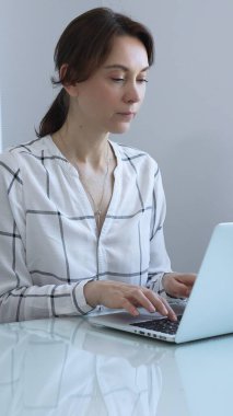 Gösterişli cam bir masada oturan odaklanmış iş kadını, parlak, modern bir ofiste dizüstü bilgisayarıyla yazı yazıyor, tamamen işine dalmış ve profesyonellik ve güven saçıyor. İş adamları konsepti