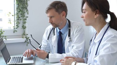 İki doktor bir dizüstü bilgisayarda tıbbi çizelgeleri inceliyor, hastane veya klinik ortamdaki hasta verilerini tartışıyorlar. Tıp ve sağlık hizmetleri kavramı