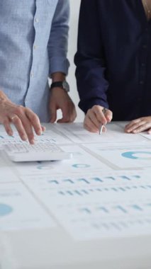 İş arkadaşları birlikte çalışıyor, finansal tabloları analiz ediyor ve bir ofis toplantısında şirket performansını tartışmak ve gelecekteki stratejileri planlamak için hesap makinesi kullanıyorlar..