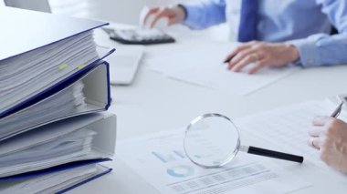 İş adamları dizüstü bilgisayar ve büyüteç kullanarak finansal verilerle çalışıyor, grafikleri analiz ediyor ve raporları kontrol ediyor, kapatıyorlar. Ticarette denetim ve vergiler.