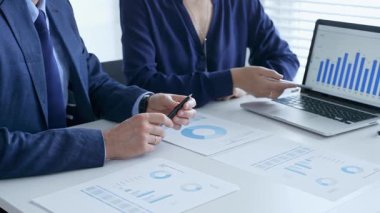 Bir proje üzerinde işbirliği yapan iş arkadaşları, dizüstü bilgisayar ve belgelerdeki mali verileri analiz ederken çizelgelere işaret ediyorlar. İş adamları ve finans kavramı