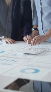 İş arkadaşları birlikte çalışıyor, finansal tabloları analiz ediyor ve bir ofis toplantısında şirket performansını tartışmak ve gelecekteki stratejileri planlamak için hesap makinesi kullanıyorlar..