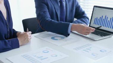 Bir proje üzerinde işbirliği yapan iş arkadaşları, bir dizüstü bilgisayar ve belgelerde yer alan mali tablolar ve grafikleri analiz ederken, bir toplantı sırasında önemli verilere işaret ediyorlar. İş adamları ve finans kavramı