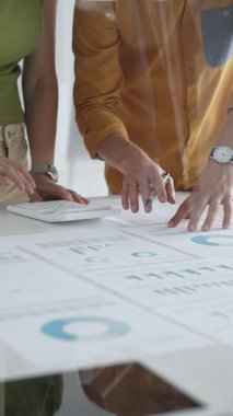 İki iş adamı bir proje üzerinde işbirliği yapıyor, bir tabloda gösterilen finansal çizelgeleri ve istatistikleri analiz ediyorlar, kesin hesaplamalar için bir hesap makinesi kullanıyorlar