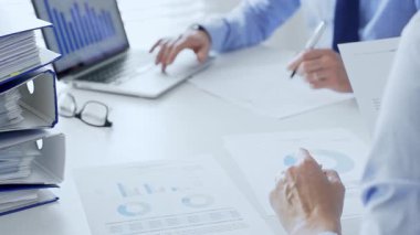 Ofis çalışanları ya da denetçiler mali raporları analiz ediyor ve ön planda bir yığın mavi klasörle beyaz masada otururken belgeleri kontrol ediyorlar. İş dünyasında denetim ve vergi teması.