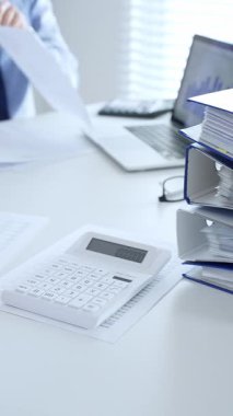 Ofis çalışanları mali raporları analiz ediyor ve ön planda evrak dolu mavi dosyalarla dolu beyaz bir masada otururken belgeleri imzalıyorlar. İş dünyasında denetim ve vergi teması