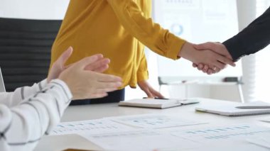 Profesyonel iş arkadaşları anlaşmayı mühürlüyor, ortaklığı alkışlarla, mali evraklarla ve başarılı iş görüşmelerini çevreleyen dijital cihazlarla kutluyorlar.