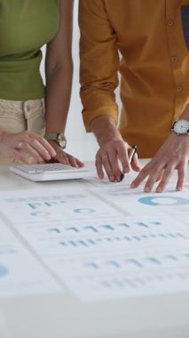 İki iş adamı bir proje üzerinde işbirliği yapıyor, bir tabloda gösterilen finansal çizelgeleri ve istatistikleri analiz ediyorlar, kesin hesaplamalar için bir hesap makinesi kullanıyorlar