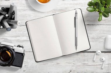 Kalemler, kahve fincanları, kulaklıklar, klasik film kamerası ve sulu bitkilerle dolu ahşap ofis masasındaki boş deri defterin üst görüntüsü. Yüksek çözünürlük.