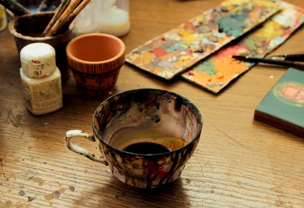 Cup covered with paint, with a wood stain substance. Artist\'s desktop. Workflow of the artist in the studio. Brushes and paints on the background in studio.