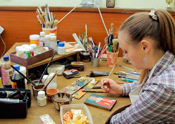 Girl artist paints a picture in the studio. Reproduction of the icon of St. Nicholas. Workflow of the artist in the studio. Brushes and paints on the background art workplace.