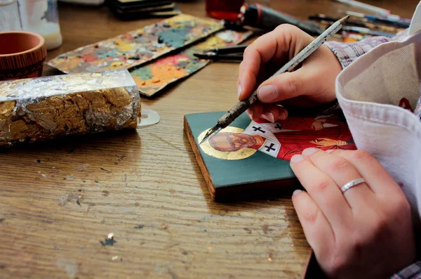 Artist paints a picture of acrylic paints. Close-up view. Artist's desktop. Reproduction of the icon of St. Nicholas. Workflow of the artist in the studio. Brushes and paints on the background art workplace.