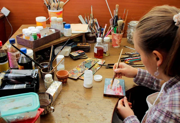 For protection wooden picture is process of applying raquelure varnish on the product. Reproduction of the icon of St. Nicholas. Girl artist paints a picture in the studio. Brushes and paints on the background workplace.