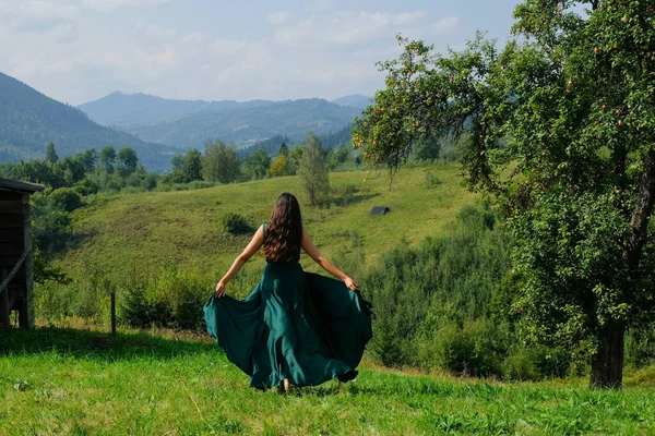 Mutlu, esmer kız çimlerde koşuyor. Arka planda Karpatlar var. Dağ yamacında uzun, ipek, yeşil elbiseli romantik Ukraynalı kadın..