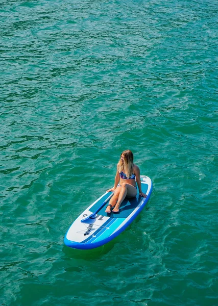 SUP Stand up paddle board. Blond girl rest on paddle board in sea. Aerial view. Woman on summer holidays vacation lifestyle. Mtsvane Kontskhi Beach, Batumi, Georgia.
