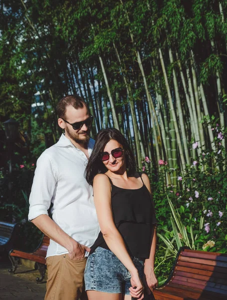 一对快乐的情侣在户外散步 背景为竹子园 微笑的男人和戴太阳镜的幸运女人在夏天过得很开心 — 图库照片