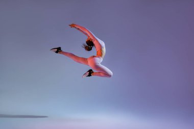 Athletic active woman jumping on studio background with colored filter. Dynamic movement