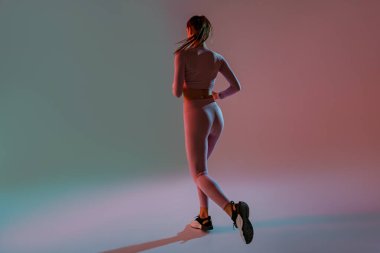 Athletic active woman wearing sportswear jumping on studio background. Dynamic movement