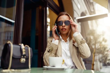 Woman sitting at cafe terrace talking on phone while drinking coffee. High quality photo