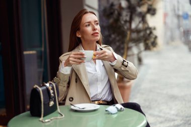 Stylish young woman drinking coffee on restaurant terrace and looking at side. High quality photo