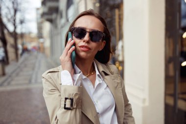 Focused businesswoman in sunglasses is talking phone on city street background . High quality photo