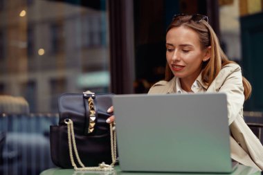 Attractive woman working on laptop online while sitting at outdoors cafe terrace. High quality photo