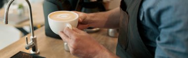 Close up of man hands standing by wooden table with cup of cappuccino