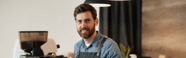 Süslü sakallı yakışıklı barista kahve dükkanında tezgahın arkasında gülümserken.