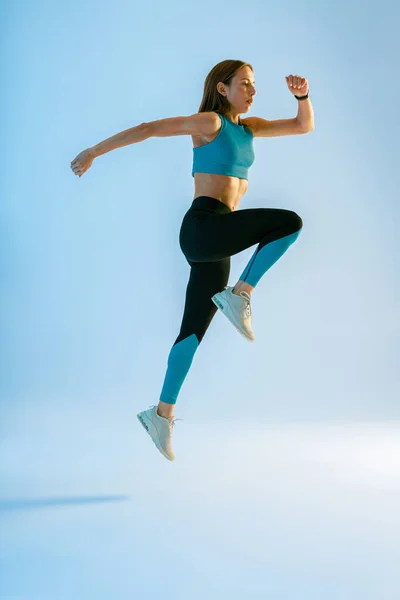 陸上競技のフィットネス女性がスタジオの背景を飛び回っています ダイナミックな動きだ 高品質の写真 — ストック写真