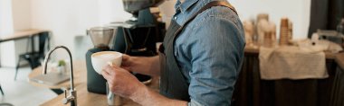 Tezgahın arkasında beklerken müşteriye vermeden önce elinde bir fincan kahve tutan yakışıklı barista.