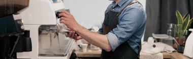 Yakışıklı barista kahve makinesini yıkıyor ve kafeteryada bir kahve tankı tutuyor.