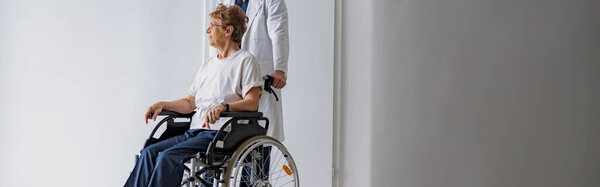 Профессиональный врач-мужчина несет пациента на инвалидной коляске в медицинском зале клиники. Высокое качество фото