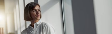 Attractive european business woman with laptop standing in modern office near window