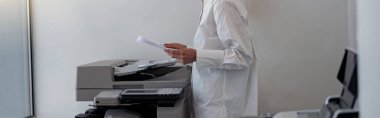 Smiling woman worker scanning a document on photocopy machine In modern office. Blurred background