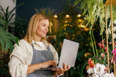 Dükkanında dizüstü bilgisayarda çalışan önlük giyen güzel bir çiçekçi.