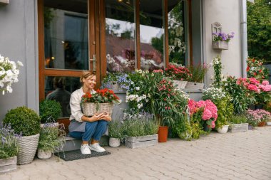 Çiçekçi kadın küçük işletme sahibi çiçekçide oturuyor ve ev bitkileriyle müşteri bekliyor.