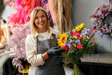 Çiçekçi kadın gülümsüyor ve elinde çiçekçide satılmaya hazır güzel bir beste tutuyor. 