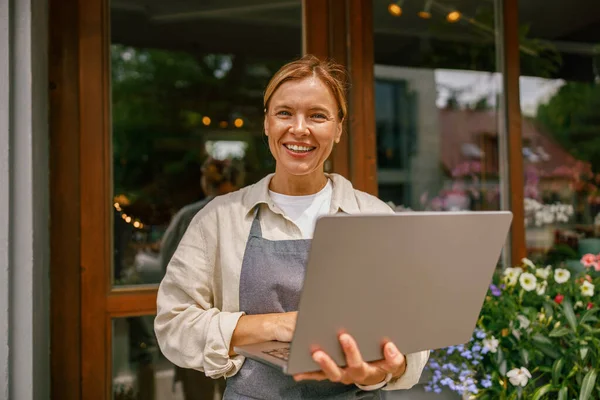 stock image Beautiful flower shop owner wearing apron working on laptop in her store