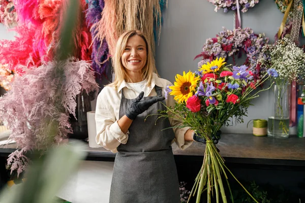 Çiçekçi kadın gülümsüyor ve elinde çiçekçide satılmaya hazır güzel bir beste tutuyor. 