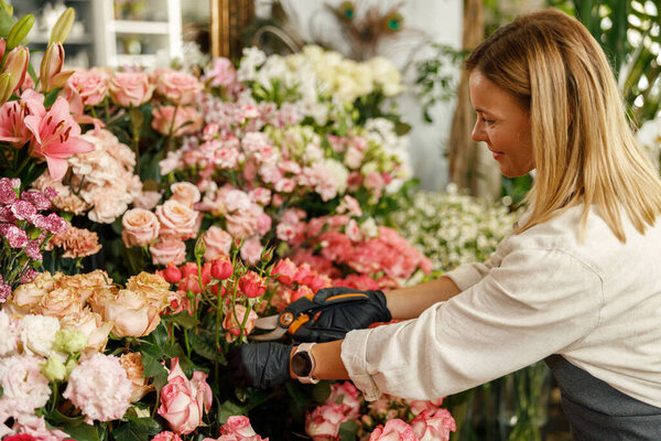 Florist in apron holding secateurs while cutting flowers in flower shop. High quality photo