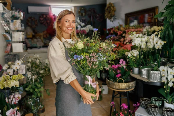 Stock image Attractive woman flower shop owner in apron holding bouquet of flowers at florist store