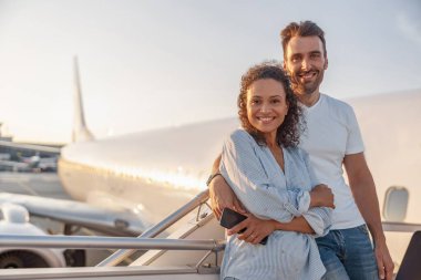 Mutlu bir çift turistin portresi, kadın ve erkek gün batımında uçağa binmeye hazırlanırken heyecanlı görünüyorlar. Tatil, yaşam tarzı, seyahat kavramı