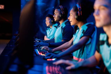 Esport oyuncularıyla birlikte oturan ve bilgisayar kulübünde video oyunu oynayan konsantre genç adama odaklanın.