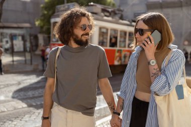 Eski tramvay geçmişi olan bir kadın, şehir caddesinde erkek arkadaşıyla yürürken telefonla konuşuyor. 