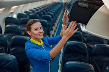 Gülümseyen kadın uçuş görevlisi, yolcu salonundayken valizini üstteki bagaj bölümüne yerleştiriyor.